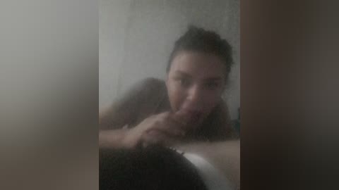 A blurry video shows a young woman with dark hair, partially nude, performing oral sex on a man's erect penis in a dimly lit, steamy shower.