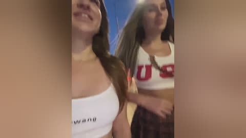 Media: A video featuring two young women with light skin, one wearing a white \"USA\" crop top and the other a plaid skirt, both smiling.