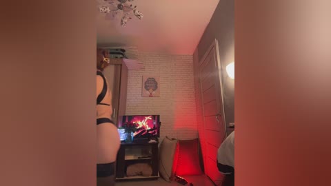 Media: A dimly lit, cozy living room with exposed brick walls, a fireplace, a TV displaying a red flame effect, and a decorative chandelier.