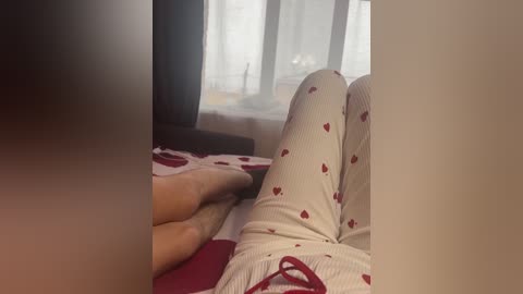 A video shows a person in white pajamas with red heart patterns, lying on a bed, with a blurred, dark figure's hand touching their leg.
