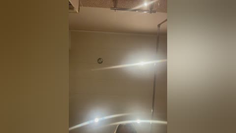 Media: A video of a dimly lit room with beige walls, featuring a small clock on the wall and bright lens flare from the camera's flash.