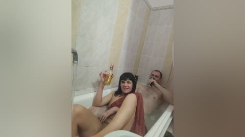 A candid video of a nude couple in a bathtub, a woman with straight black hair and a man with a shaved head, both holding drinks, smiling.