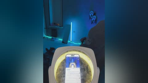 Video of a VR headset showing a computer screen with a blue interface; dimly lit, modern room with neon blue lighting, minimalistic decor, and a bed in the background.