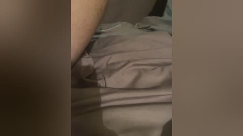 Video of a close-up, dimly lit scene showing a person's arm and leg partially covered by grey sheets. The skin tone is light, and the sheets appear soft and smooth.