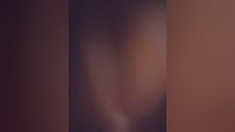 A blurry video of a person's face, likely female, with medium skin tone, partially obscured by shadows and a dark background, creating a mysterious and intimate atmosphere.