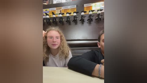 Media: A video of two young girls with curly hair, one in a white t-shirt, seated at a table in a cafeteria, surrounded by shelves of boxed lunches.