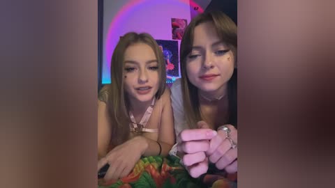 Media: Video of two young women with fair skin and long brown hair, wearing casual clothing, playing with a stuffed animal in a cozy, dimly-lit room.