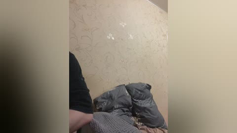 Video of a person wearing a black shirt and grey knit hat, kneeling on a beige-patterned carpet, with a grey blanket and jacket beside them.