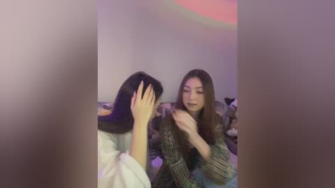 Media: A blurred video shows two young women, one with long hair, wearing a patterned shirt, covering her face with her hand, while the other, also with long hair, wears a checkered shirt, sitting beside her.