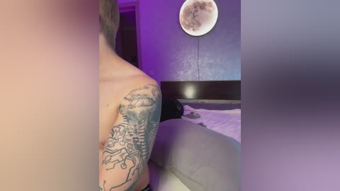 Media: Video of a man with a detailed, black-and-gray tattoo of a dragon on his left shoulder, standing in a dimly lit bedroom with a full moon moon-shaped light on the wall.