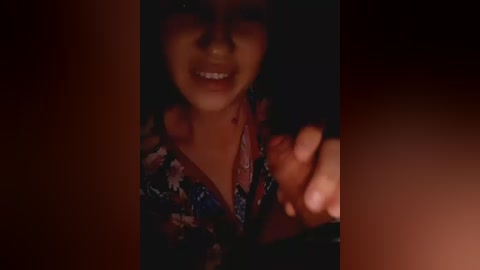Video of a young woman with dark hair and a wide, bloody smile, holding a knife, set in a dimly lit room.