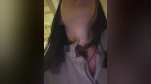 Media: Video of a close-up of a woman with fair skin, black hair, and a gray sweater, leaning forward, blurred background.