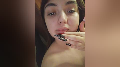 Media: Video of a young woman with light brown skin, dark hair, and large, almond-shaped eyes. She has a natural makeup look with a hint of gloss on her lips. Her manicured nails are adorned with intricate black and white nail art.