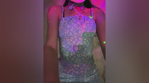 A video of a woman with light skin wearing a sheer, floral-patterned dress, standing in a dimly lit room with purple and pink lighting. Her black hair is wet and sticking to her face.