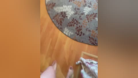 Video of a wooden floor with a floral rug in muted tones, featuring a person in a floral-patterned dress, viewed from above.
