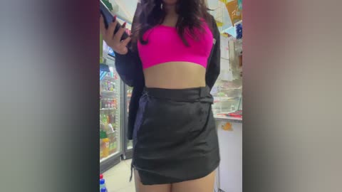 Media: Video of a young woman with long dark hair in a bright pink sports bra and black skirt, taking a selfie in a well-lit convenience store.