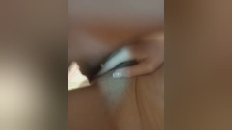 A blurry video shows a person's hand holding a teal-colored object against a beige background, possibly a phone or a remote control.