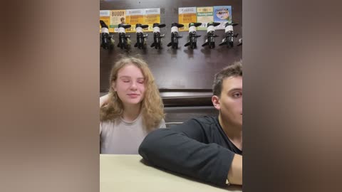 Media: Video of a blonde woman with curly hair wearing a white top, seated next to a man in a black shirt, in a dimly-lit cafe with mounted bicycle signs on the wall.