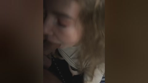Media: Video of a close-up, blurred face of a blonde woman with a neutral expression, likely in a dimly lit room.