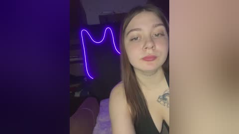 Media: Video of a young woman with fair skin, long brown hair, and light makeup, wearing a black top, in a dimly lit room with neon lights and a tattoo on her neck.
