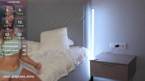 A video shows a woman in light blue lingerie standing beside a bed with white sheets, in a dimly lit bedroom. Text overlays indicate a social media live stream.