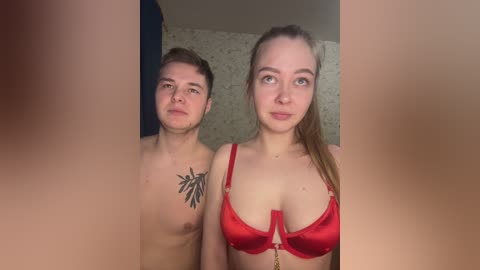 Video of a topless young man with a leaf tattoo on his chest and a woman in a red bra standing close in a dimly lit room.