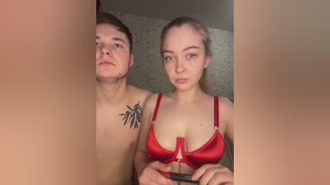 A video shows a shirtless young man with a tribal tattoo on his chest, standing beside a woman wearing a red bra, both looking serious.