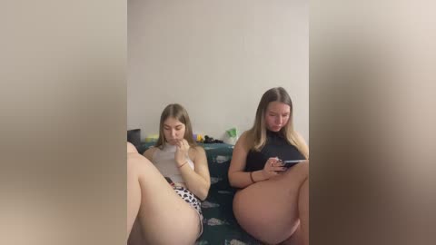 Video of two pregnant women, one Caucasian with long brown hair, the other Caucasian with long blonde hair, both seated on a couch, watching a tablet, in a dimly lit room.