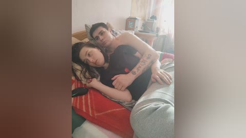 Video of a sleeping couple in a dimly lit bedroom. The woman, with dark hair, is on her side, and the man, with tattoos, embraces her from behind.