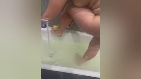 Video of a person pouring a yellow liquid into a white bathtub, with visible hand and foot. The bathtub is filled with water, and the person's skin tone is light.