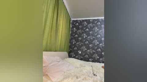 Media: Video of a modern bedroom featuring a white bed with light pink sheets, a green curtain, and a black floral wallpaper backdrop.