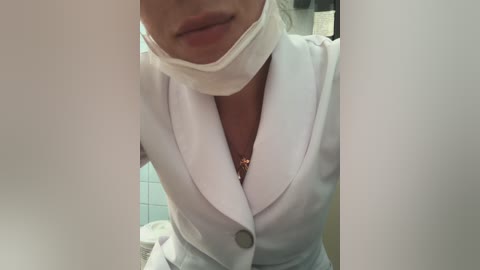 Media: Video of a person in a white lab coat with a white face mask, standing in a tiled bathroom with a toilet visible in the background.