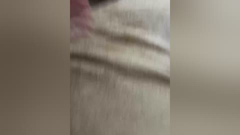 A blurred video of a person's upper body in a white, textured shirt, with faint pink and green patterns, possibly in a casual setting. The background is indistinct and out of focus.