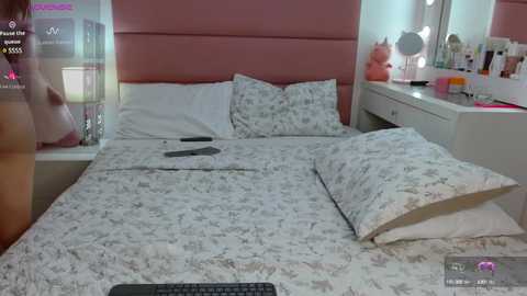 Video of a modern bedroom with a pink upholstered headboard, floral-patterned bedding, a white vanity with makeup, and a plush pink teddy bear.