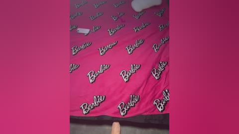 Media: A video of a bed with a bright pink Barbie-themed sheet featuring the \"Barbie\" logo in white text, slightly crumpled.