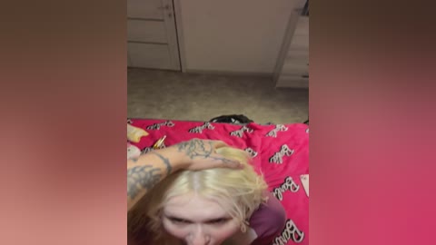 Media: Video of a blonde woman with tattoos on her arm, lying on a bed with red leopard-print sheets, wearing a purple top, with a person's hand gently resting on her head.