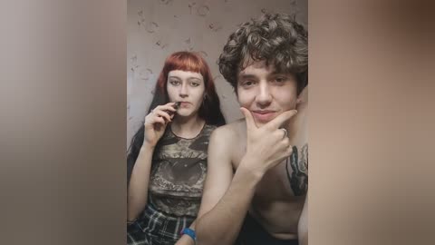 Media: Video of a young couple in a dimly lit bathroom, with the man shirtless, revealing tattoos, and the woman wearing a plaid skirt and a graphic tank top, both smiling.