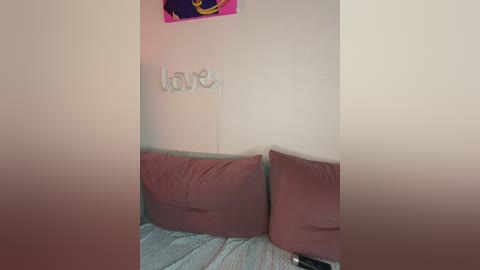 Video of a cozy corner with a beige wall adorned with \"Love\" in gold letters, a pink cushioned couch, and a colorful, abstract painting above.