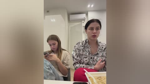 Media: Video of two young women sitting in a modern, minimalistic room; one is texting, the other is looking at a laptop.