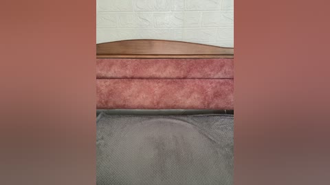 Video of a bed with a wooden headboard and a pink and gray striped bedspread. The background features a white brick wall.