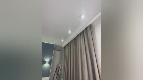 Media: Video of a modern room with beige walls, a ceiling with recessed lights, and a floor-to-ceiling curtain in a similar shade. The room features a minimalist design with a sleek, contemporary aesthetic.