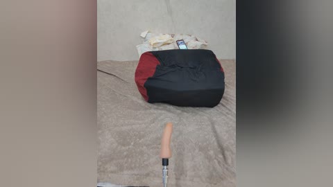 A video of a beige wall with a partially opened black and red bean bag, a metal bat, and a rolled-up mat on a light brown carpet.