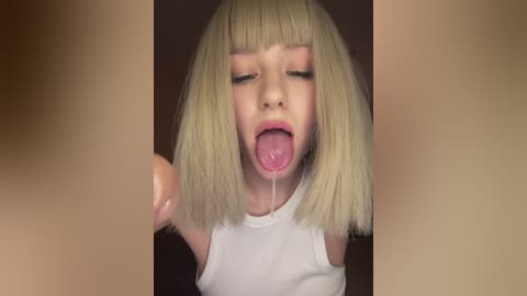 Media: Video of a blonde, light-skinned child with straight bangs and a white tank top, sticking out her tongue and drooling, framed by blurred, brownish images.