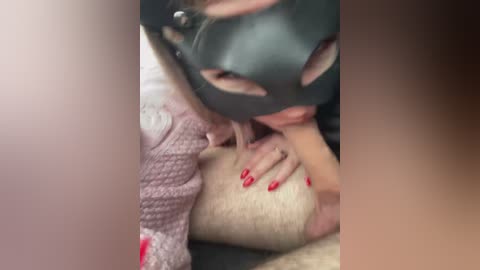 Video of a woman in a black mask, kneeling over a man's erect penis, with her hand on his thigh, wearing a pink sweater.