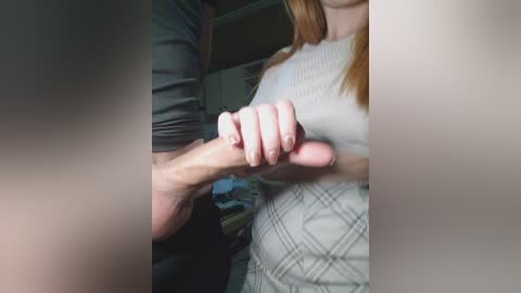 A video shows a woman in a grey sweater holding a man's erect penis; the background is blurred and dimly lit.