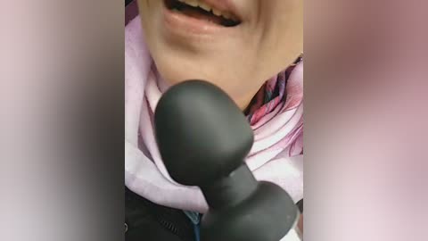 A close-up video of a person with light skin, wearing a pink and white striped shirt, holding a black microphone. The image is slightly blurred and cropped, focusing on the person's mouth and upper chest.