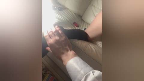 A video shows a light-skinned person's legs and hands wearing black socks and a white shirt, reclining on a beige leather couch with a remote control nearby.
