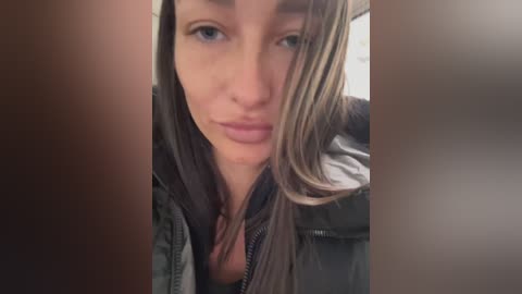 Media: A close-up video of a Caucasian woman with light brown hair, wearing a black jacket, making a pouty face. The image is blurry, with brown vertical streaks obscuring the background.