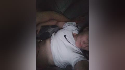 A video shows a man lying on his back, shirt lifted, exposing his bare torso and a tattoo. He is wearing dark shorts. The background is dimly lit.