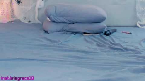 A video showing a woman lying on a bed with light blue sheets, wearing a pink and white lace bra, and a black dildo.